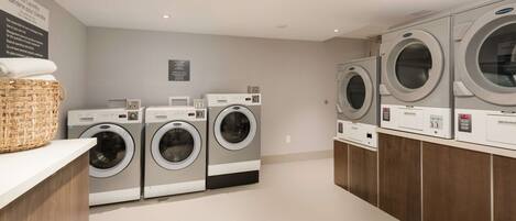A laundry area with multiple washing machines, a basket of folded towels, and a sign with instructions.
