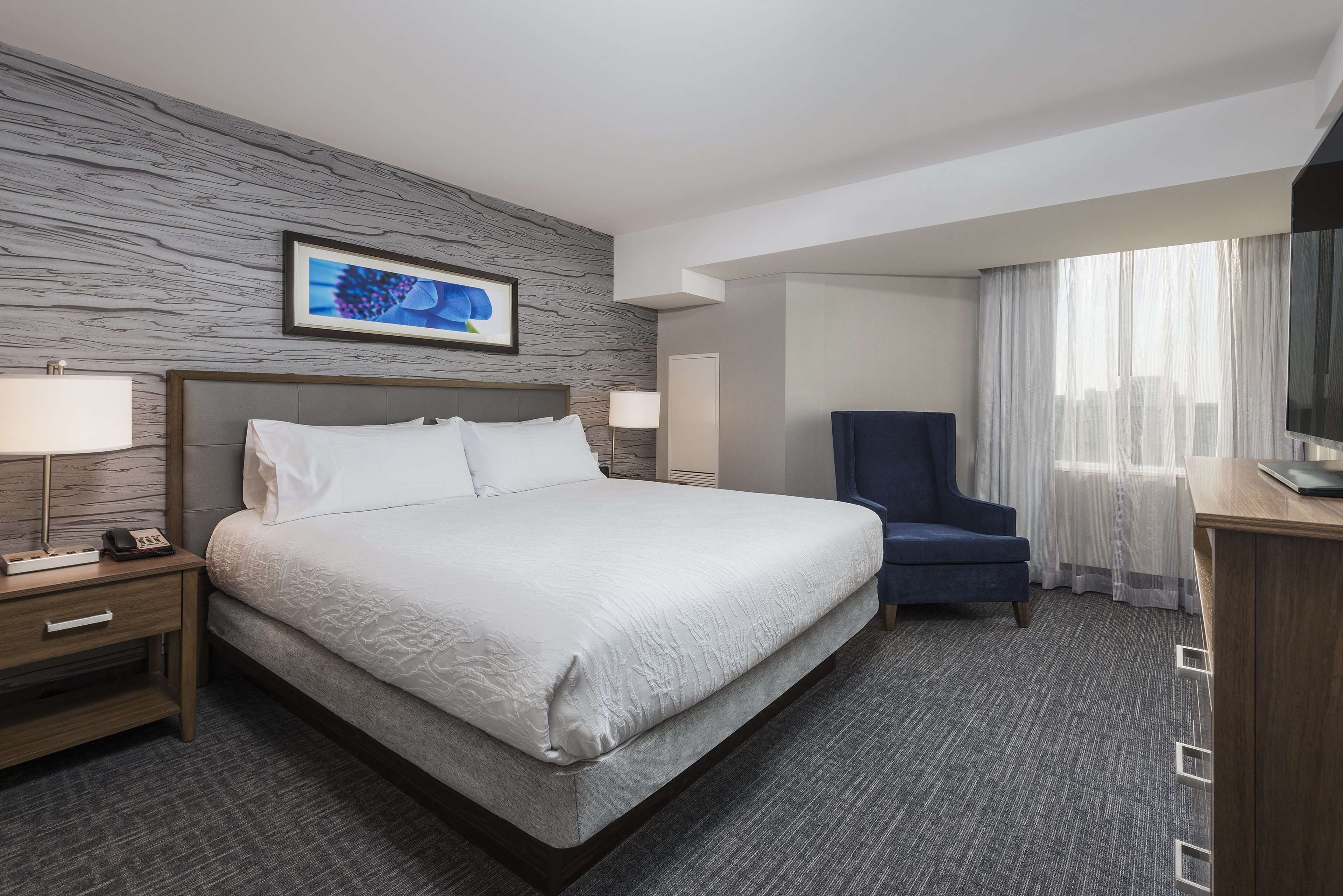 A hotel room with a large bed, a desk with a chair, a television, and a window with curtains.