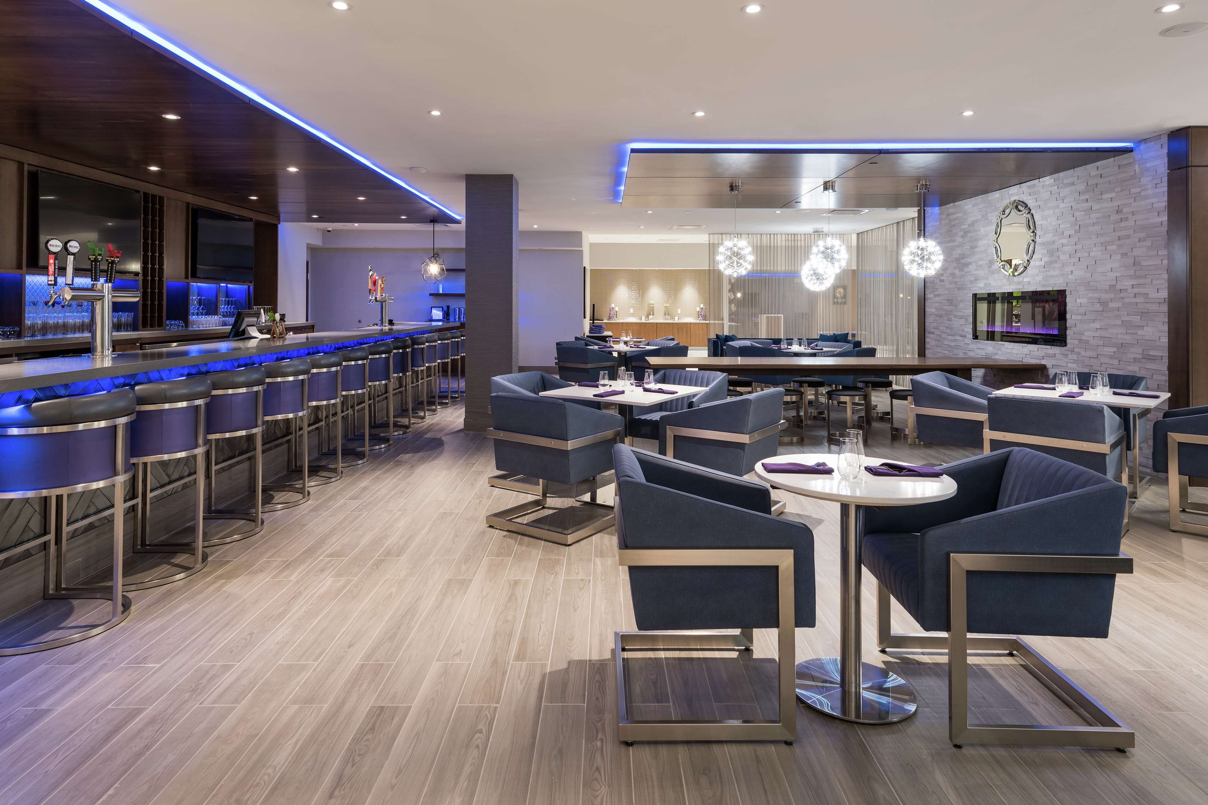Un moderno bar con una barra larga, varios taburetes y una zona de estar con mesas redondas y sillas.