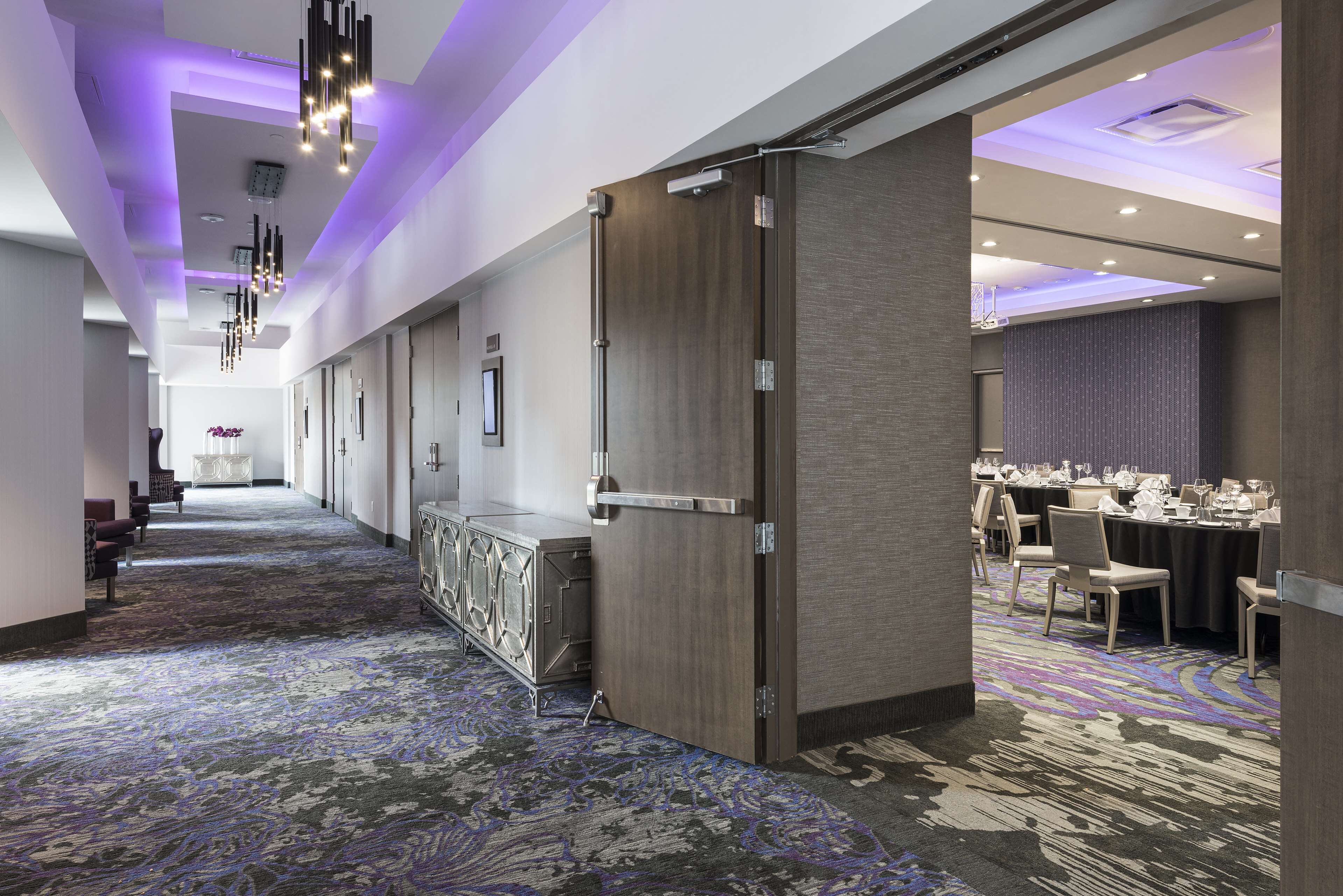 A hotel corridor with a patterned carpet, a reception area with a counter, and a dining area with tables set for a meal.