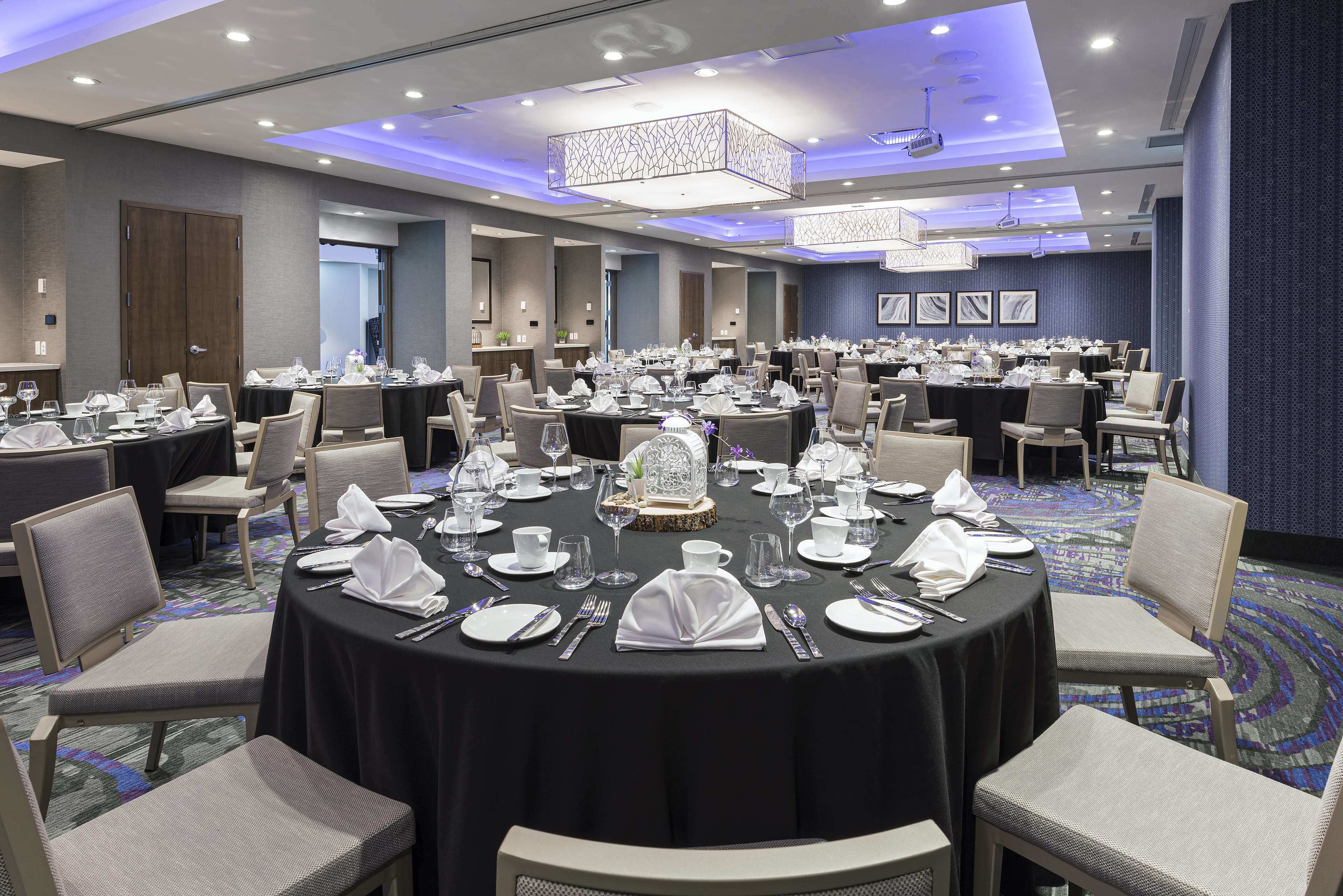 Une grande salle de conférence dotée de tables rondes aménagées pour les repas, de chaises et d’un lustre.