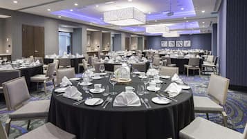 Un amplio salón de conferencias con mesas redondas dispuestas para comer, equipado con sillas y un candelabro.