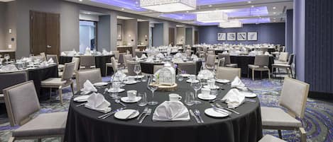 Une grande salle de conférence dotée de tables rondes aménagées pour les repas, de chaises et d’un lustre.