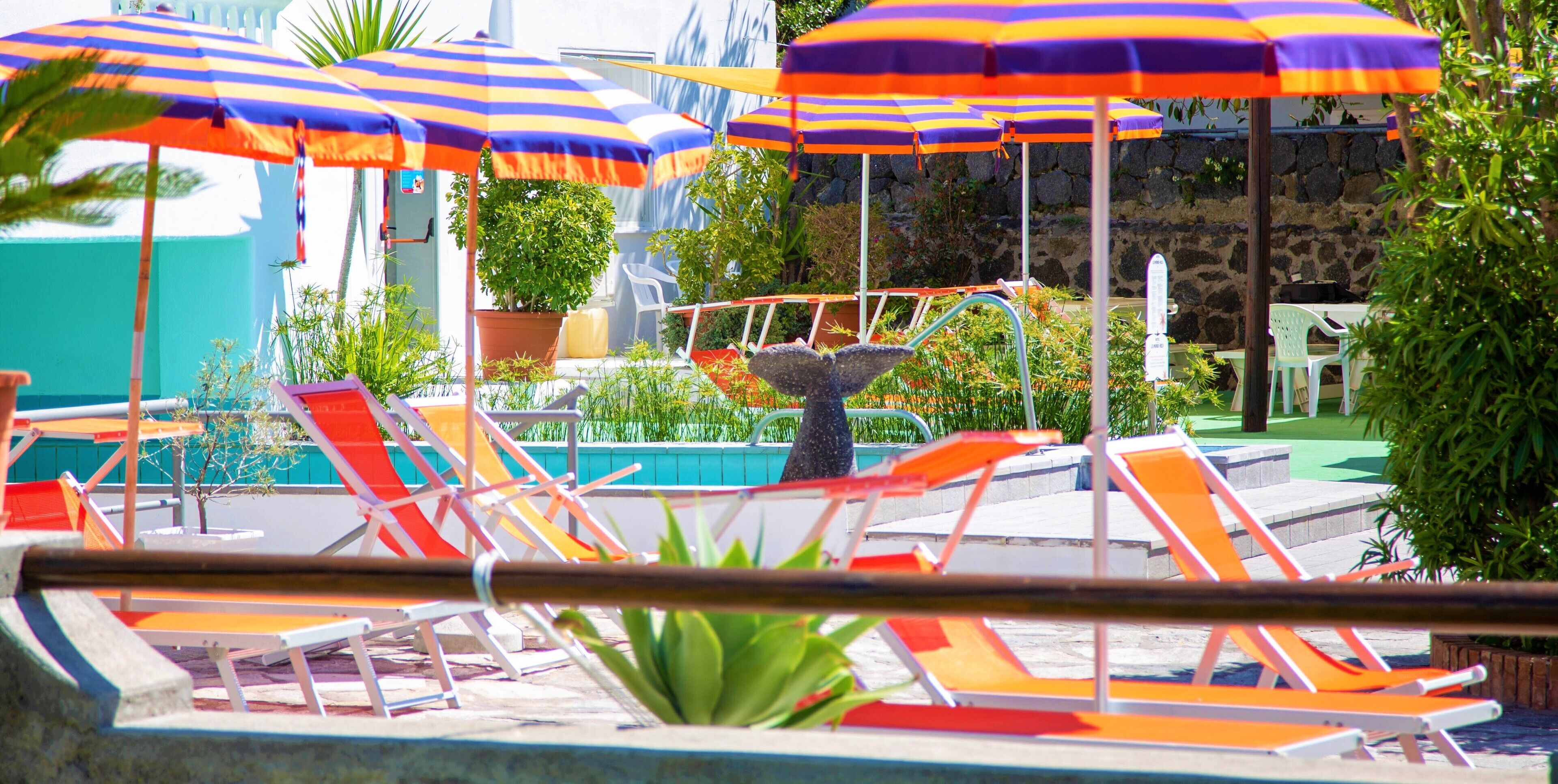 Zona junto a la piscina con sillas de descanso y sombrillas a rayas.