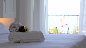 A neatly made bed with a rolled white towel and a flower, a white door, and a balcony with a table and chairs. - Hotel La Mandorla (Barano d'Ischia)