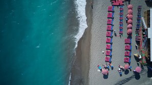 An aerial view of a beach with rows of beach chairs and umbrellas, a lifeguard tower, and a building with a sign. - Hotel La Mandorla (Barano d'Ischia)