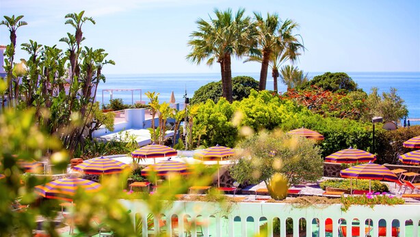 A resort with multiple colorful umbrellas, palm trees, and a pool area. - Hotel La Mandorla (Barano d'Ischia)