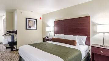 A hotel room with a large bed, a nightstand with a lamp, a dresser, and a framed picture on the wall.