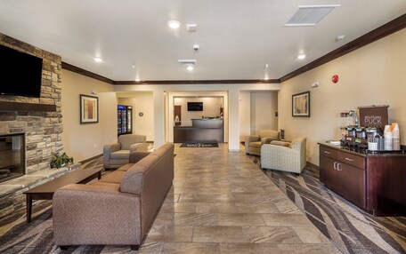 A spacious lobby with a stone fireplace, comfortable seating, a coffee station, and a reception desk.