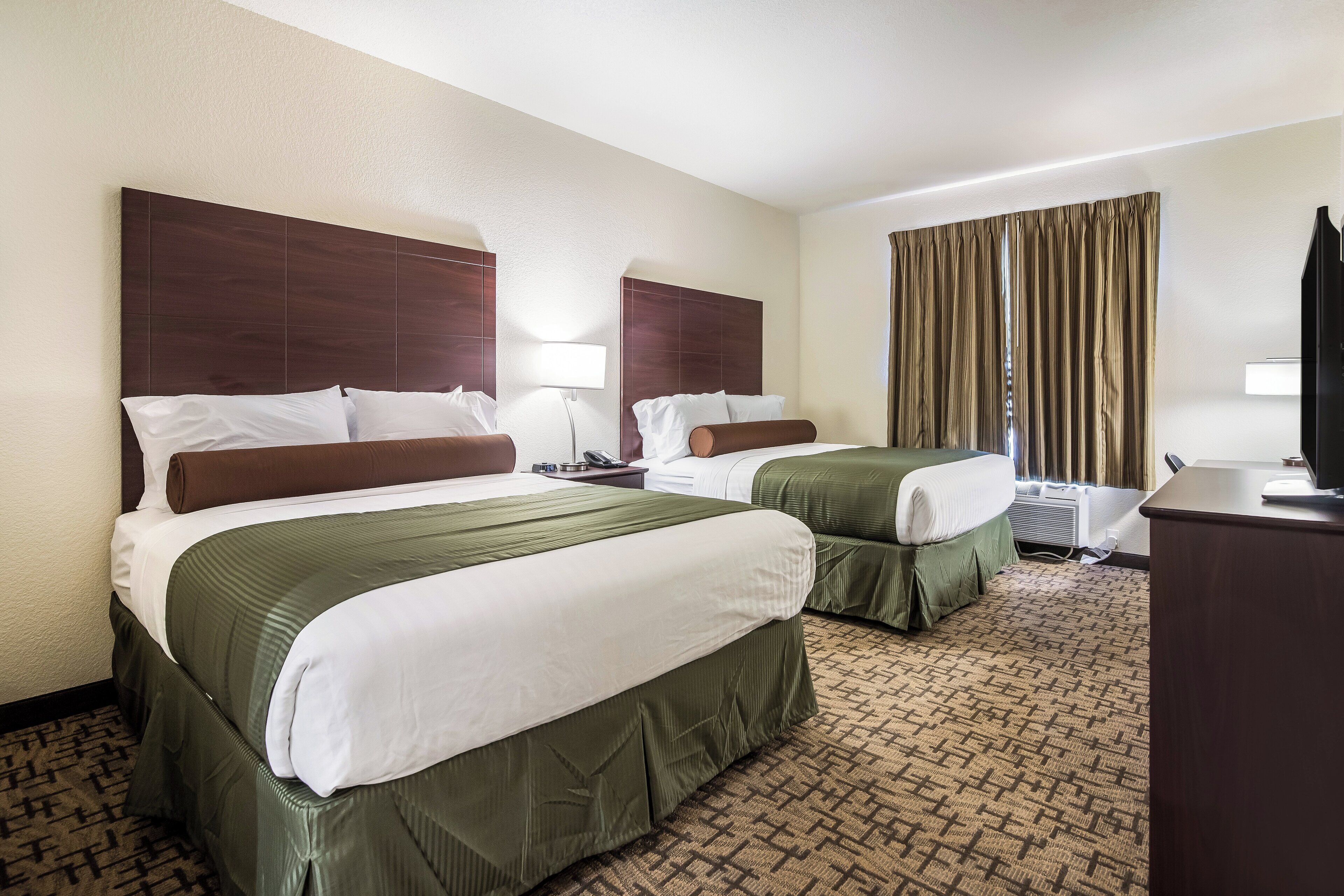 A hotel room with two beds, a desk, a TV, and a window with curtains.