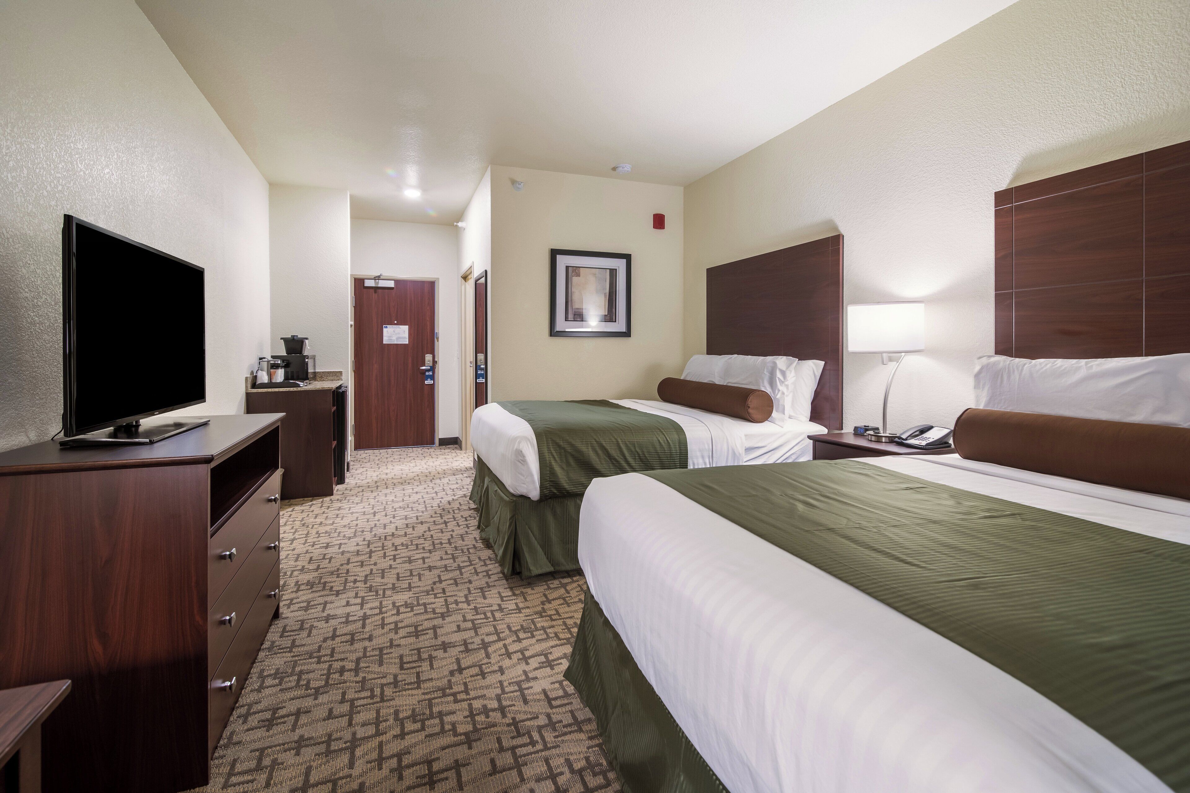 A hotel room with two beds, a TV, a desk, and a bathroom visible in the background.