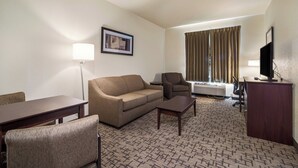 Quarto de hotel com sofá, poltrona, escrivaninha e televisão.