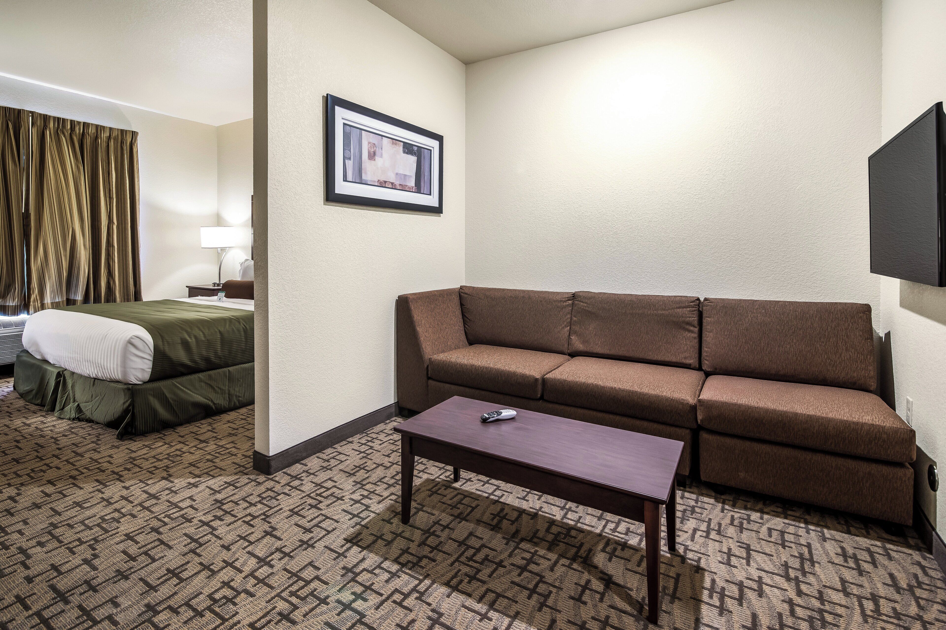 A hotel room with a bed, a sofa, a coffee table, a framed picture on the wall, and a flat-screen TV mounted on the wall.