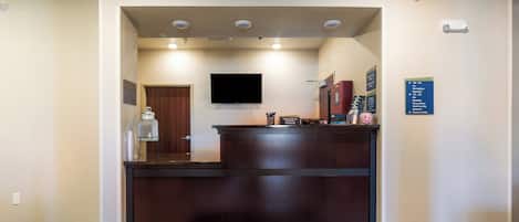 Zona de recepción de un hotel con mostrador, televisor montado en la pared y un cartel que indica la ubicación del centro de negocios.