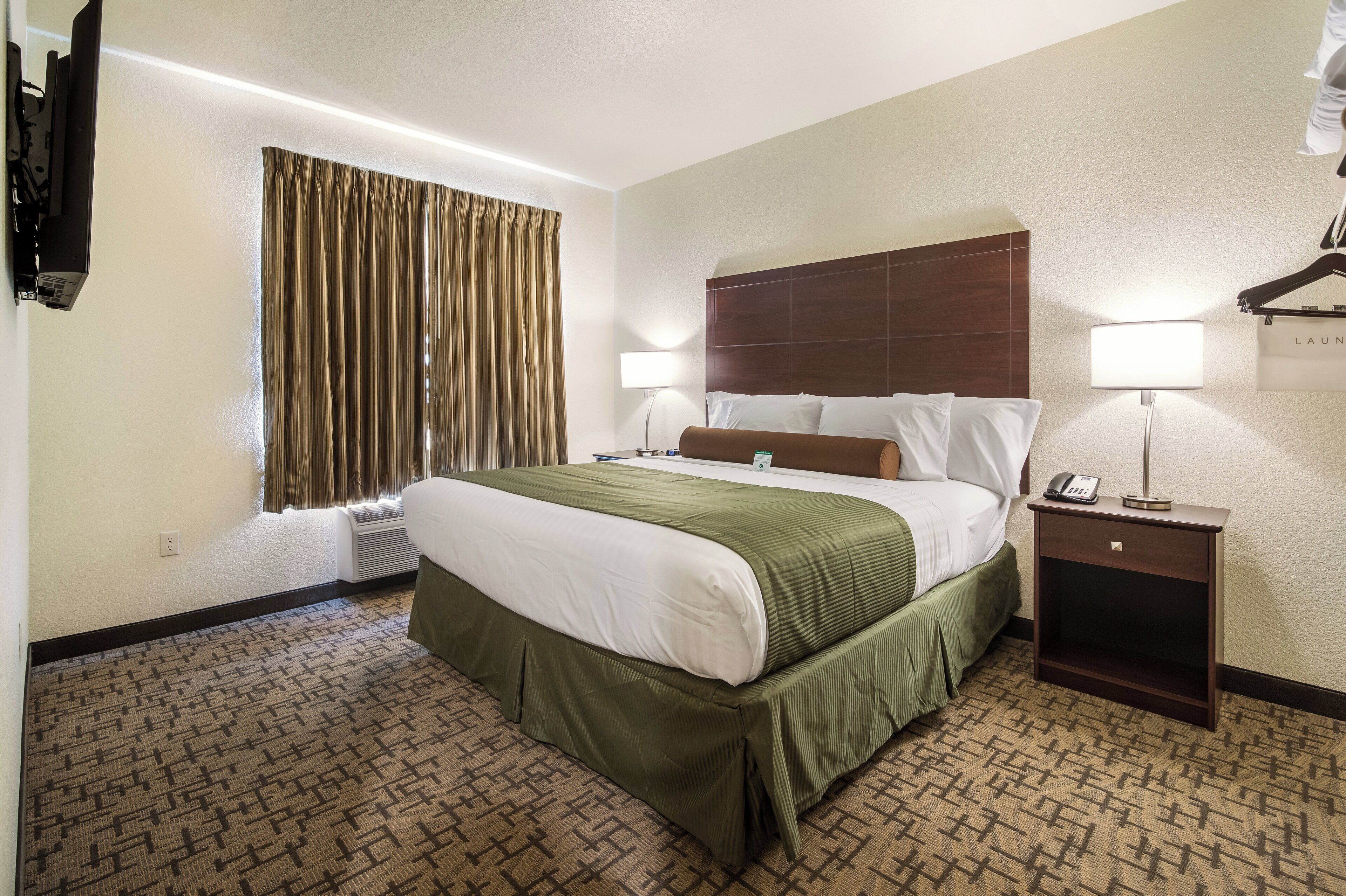 Een hotelkamer met een groot bed, twee nachtkastjes, een wandgemonteerde flatscreen televisie en een raam met gordijnen.