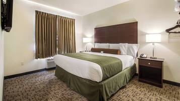 A hotel room with a large bed, two bedside tables, a flat-screen TV mounted on the wall, and a window with curtains.