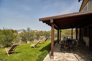 A covered outdoor patio with a stone floor, wooden furniture, and a view of the countryside.