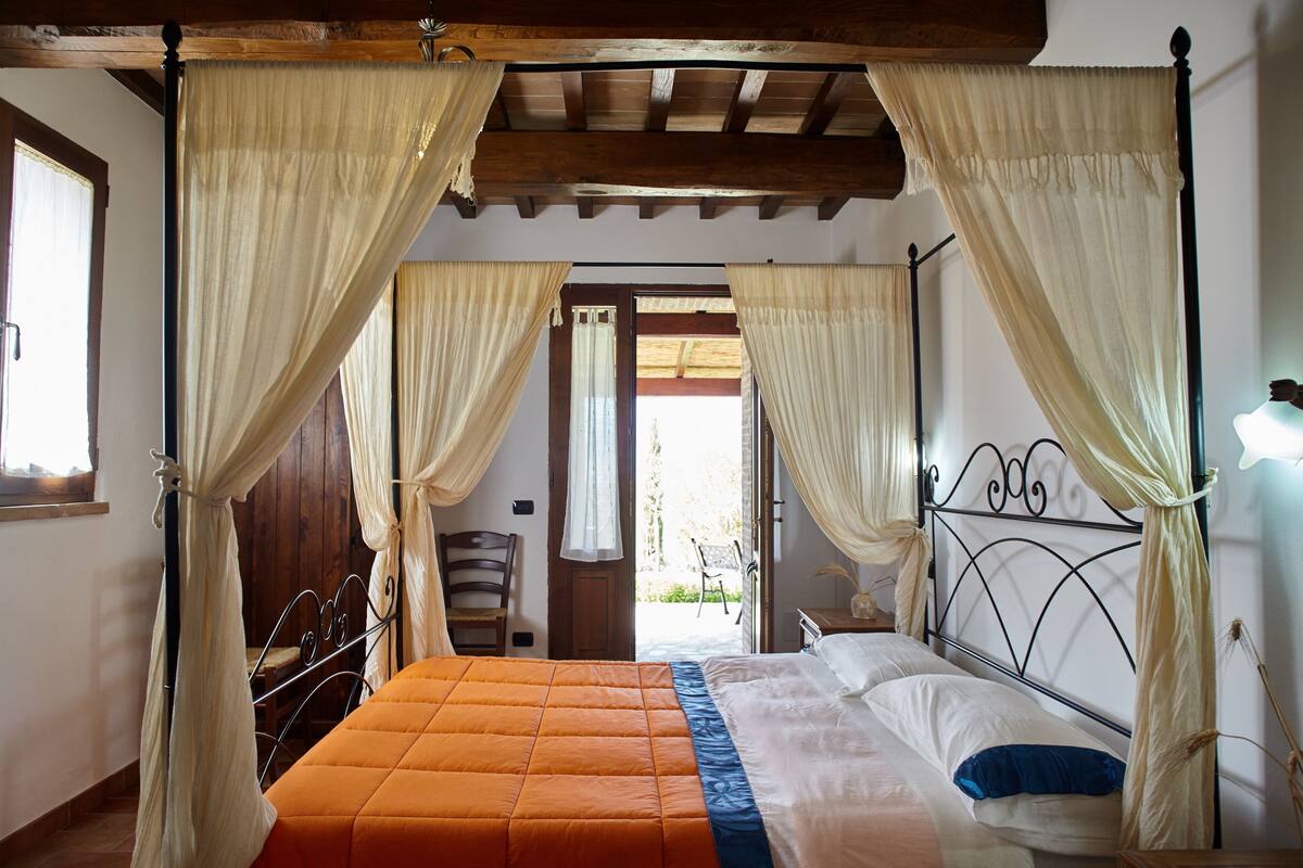 A bedroom with a four-poster bed, curtains, and a wooden ceiling.