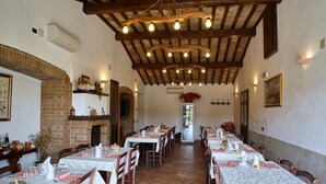 A dining area with multiple tables set for guests, wooden beams on the ceiling, and a brick fireplace. - Sant'Apollinare (Piancastagnaio)