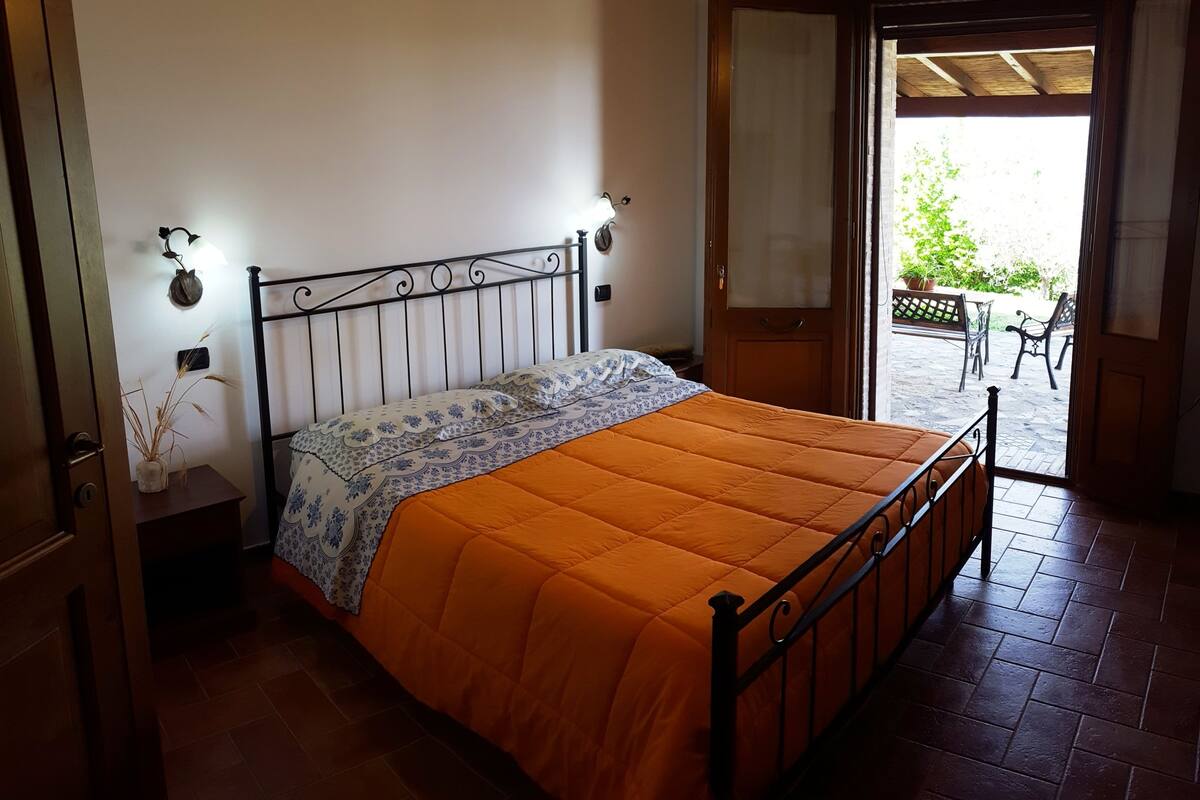 A bedroom with a bed, a nightstand, a wall-mounted lamp, and a door leading to a balcony.