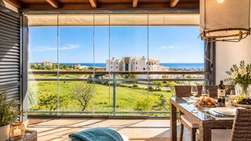 Un balcón con mesa dispuesta para comer, con vista a un paisaje costero con edificios y vegetación.