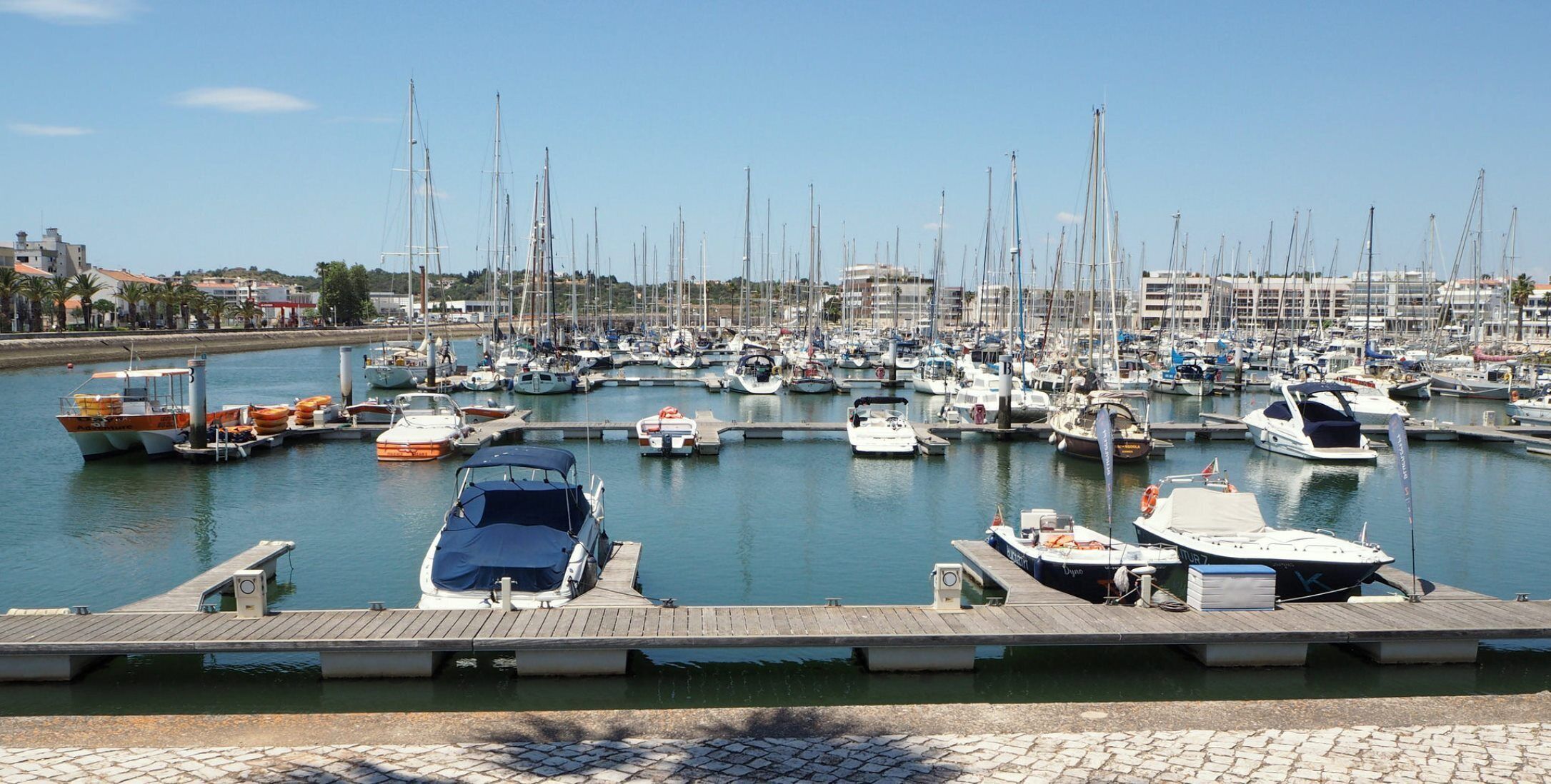 Een jachthaven met diverse boten afgemeerd, een houten steiger en een heldere lucht.