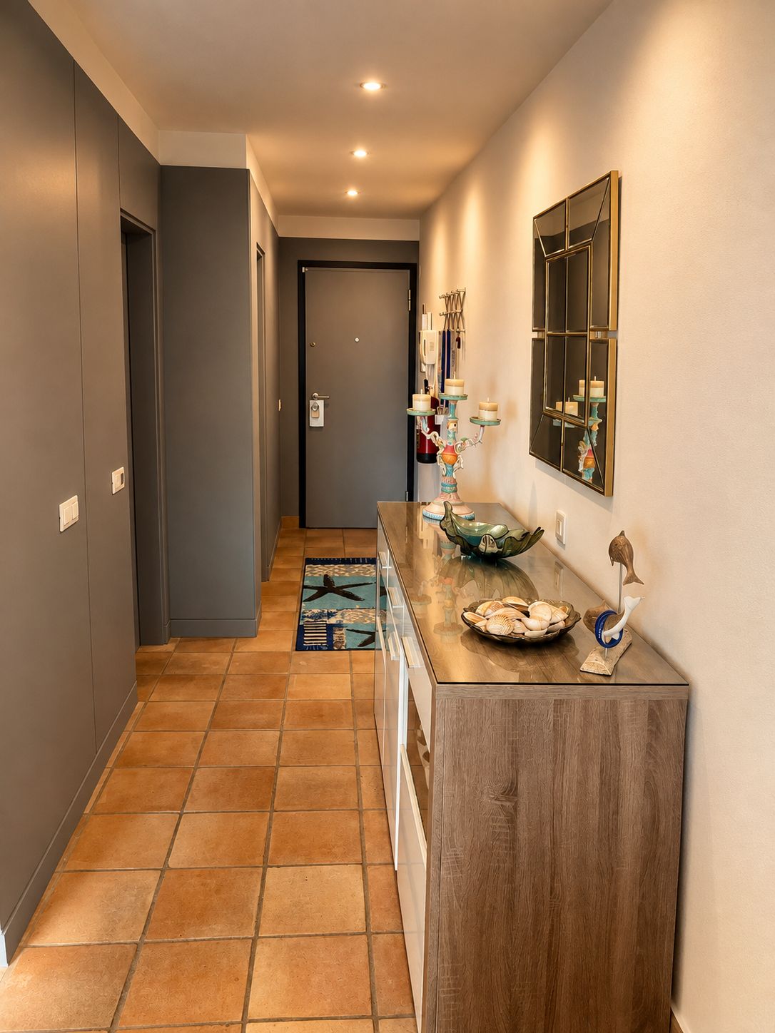A hallway with a wooden console table, a tiled floor, and a door at the end.