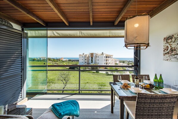 Un balcón con mesa lista para comer, una lámpara colgante y vistas de edificios sobre un paisaje verde.