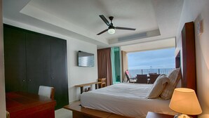 A hotel room with a bed, a desk, a chair, a ceiling fan, and a view of the sky. - Wake Up To Sounds Of The Ocean Condo (Puerto Vallarta)