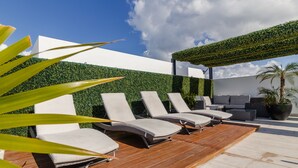 Un espacio lounge moderno al aire libre con cuatro sillones, una terraza de madera y un muro cubierto de vegetación.