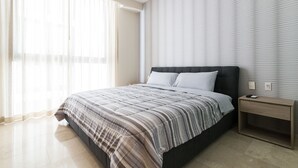 Un dormitorio moderno con una cama grande, una mesita de noche y una ventana con cortinas ligeras.