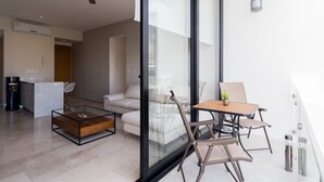 Una sala de estar moderna con un separador de vidrio, un ventilador de techo, una zona de cocina y un balcón con mesa y sillas.