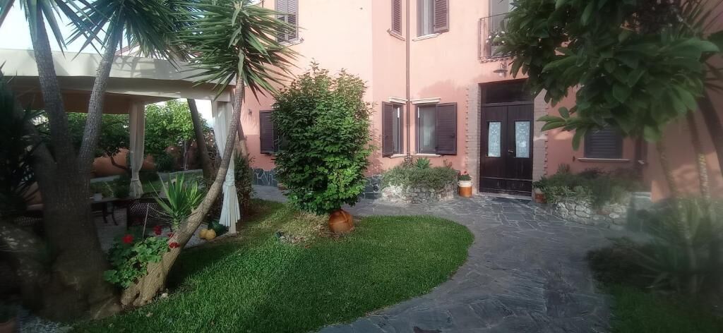 A courtyard with a paved path, a palm tree, and a building with a pink facade.
