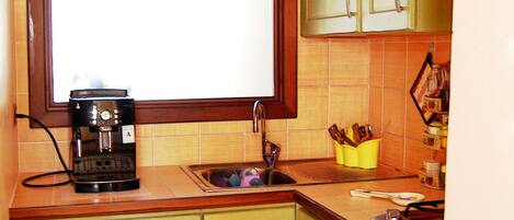 A small kitchen with green cabinets, a coffee maker, and a window with a decorative design.