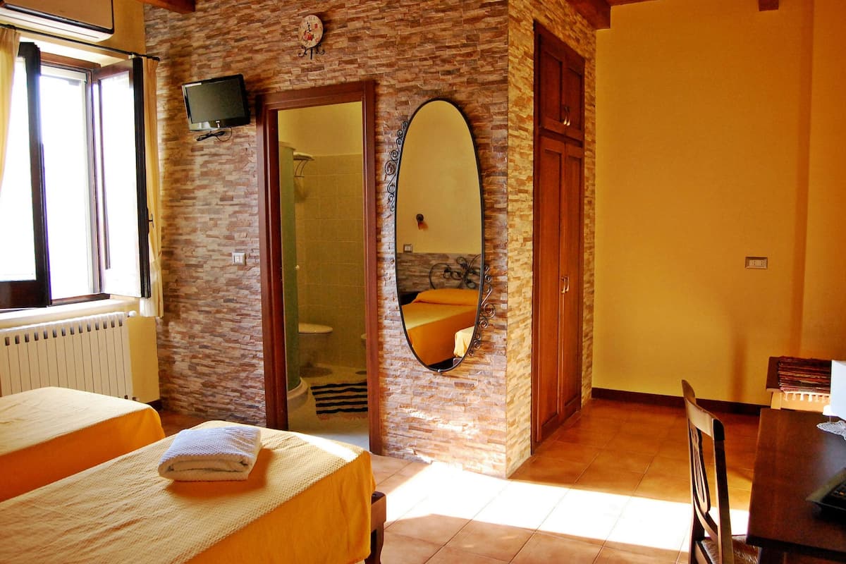 Habitación de hotel con pared de piedra, cama, baño con espejo y televisor fijado a la pared.
