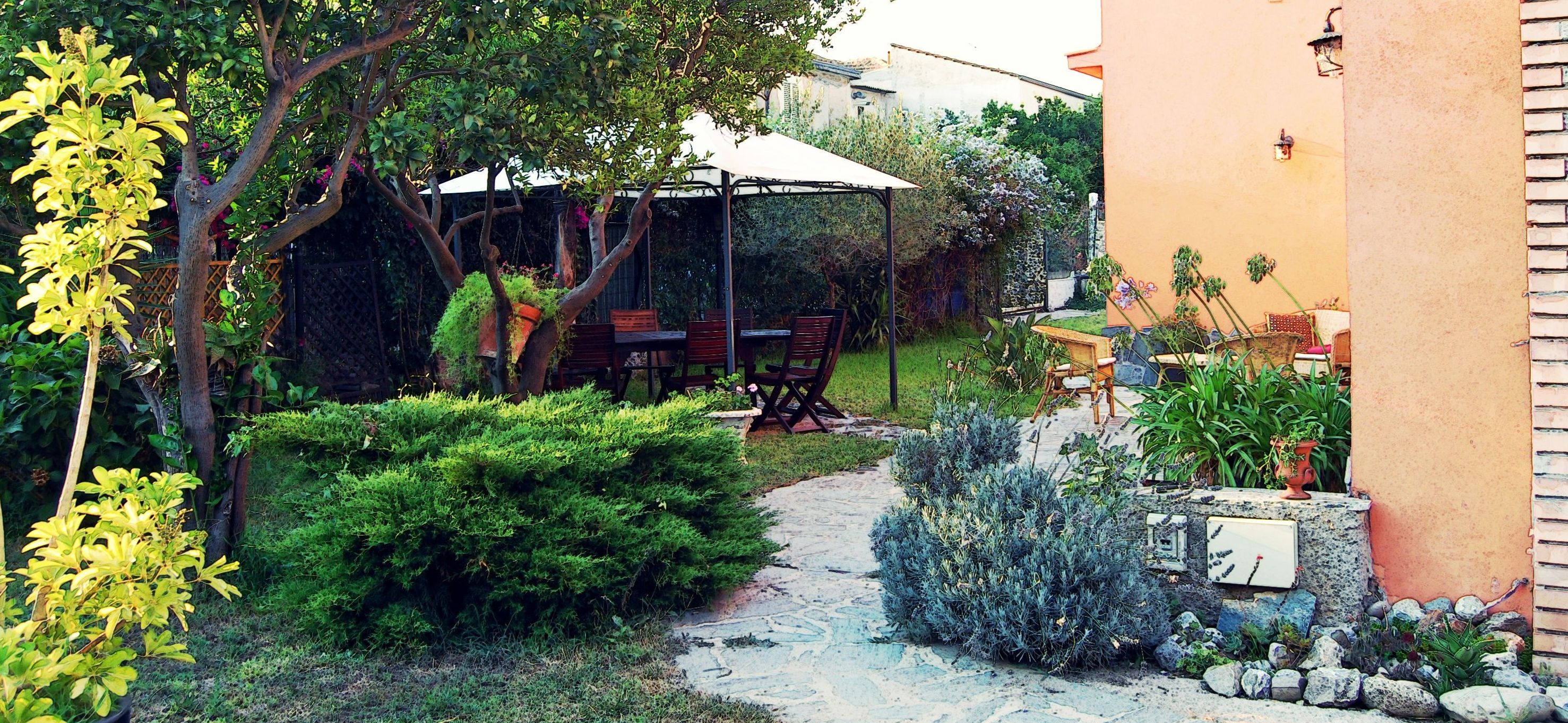 A garden with a pathway, a wooden table, and chairs under a white umbrella.