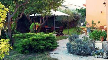 A garden with a pathway, a wooden table, and chairs under a white umbrella.