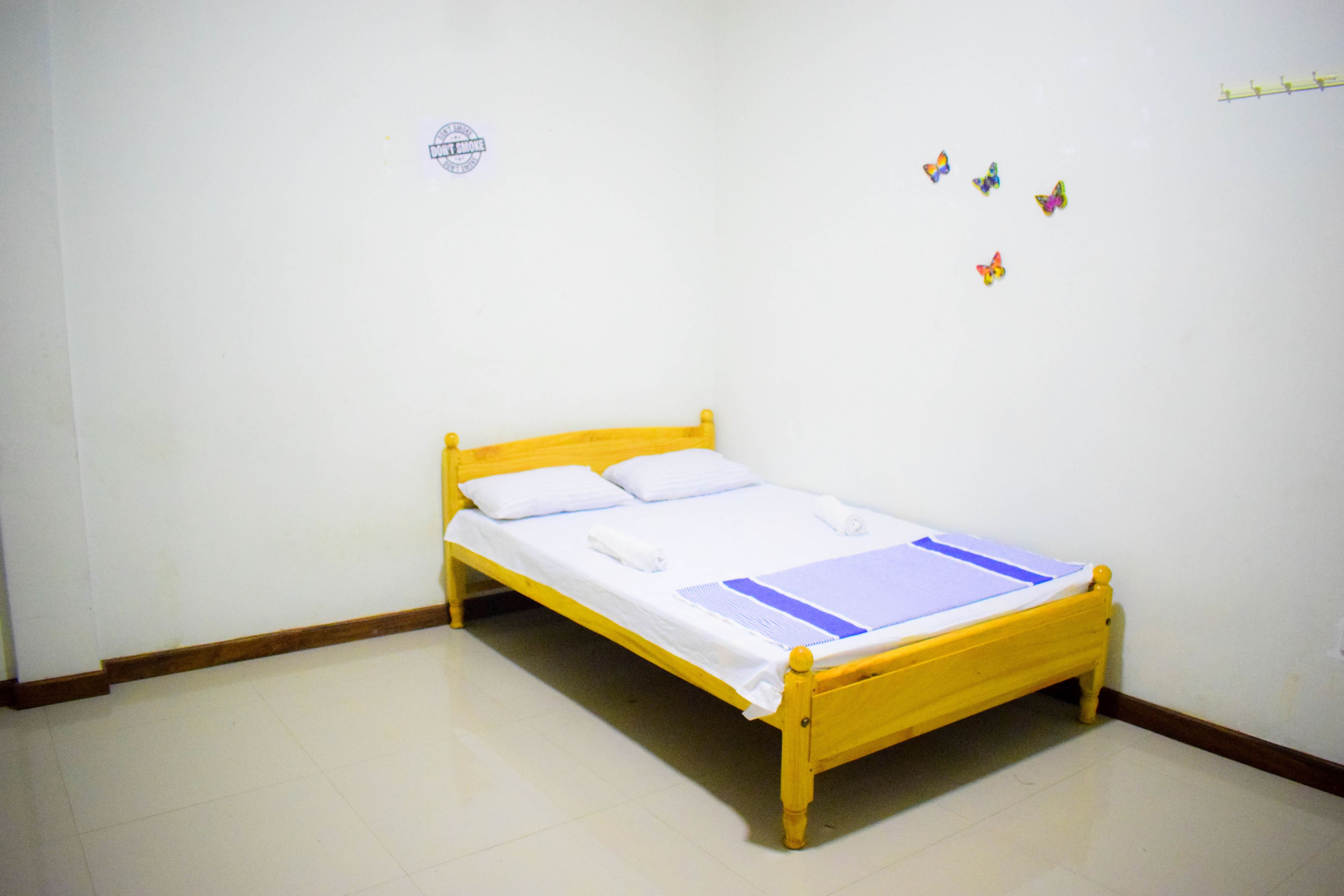 A single yellow wooden bed with white bedding in a room with white walls and a white floor.