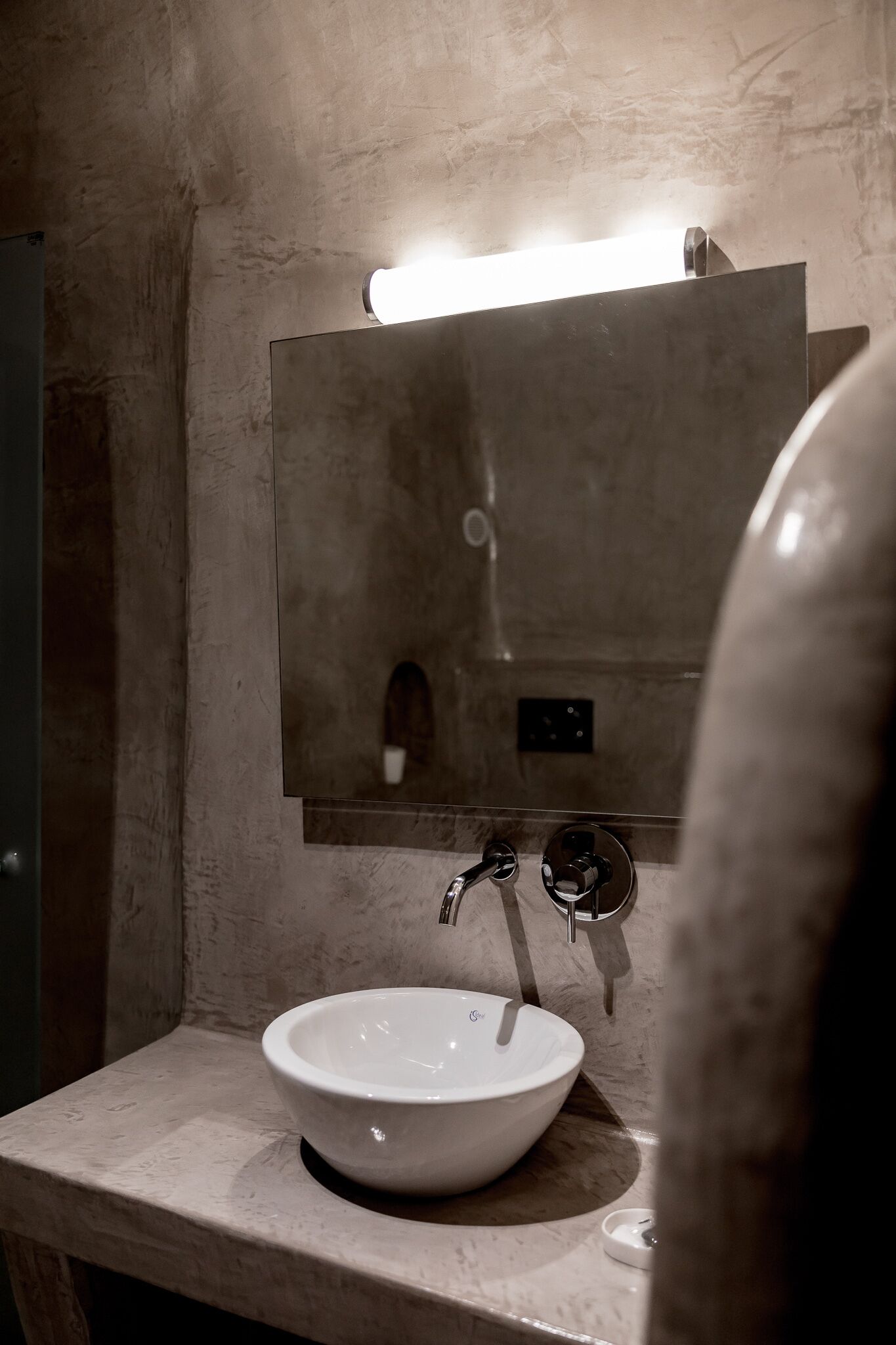 Une salle de bain avec un lavabo blanc, un miroir et un luminaire placé au-dessus du miroir.
