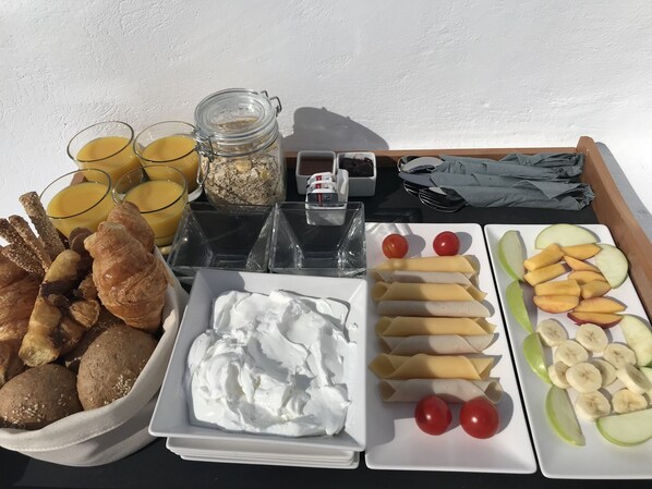 Un plateau de petit-déjeuner avec des croissants, du yaourt, des pommes, des bananes et du jus de fruits.