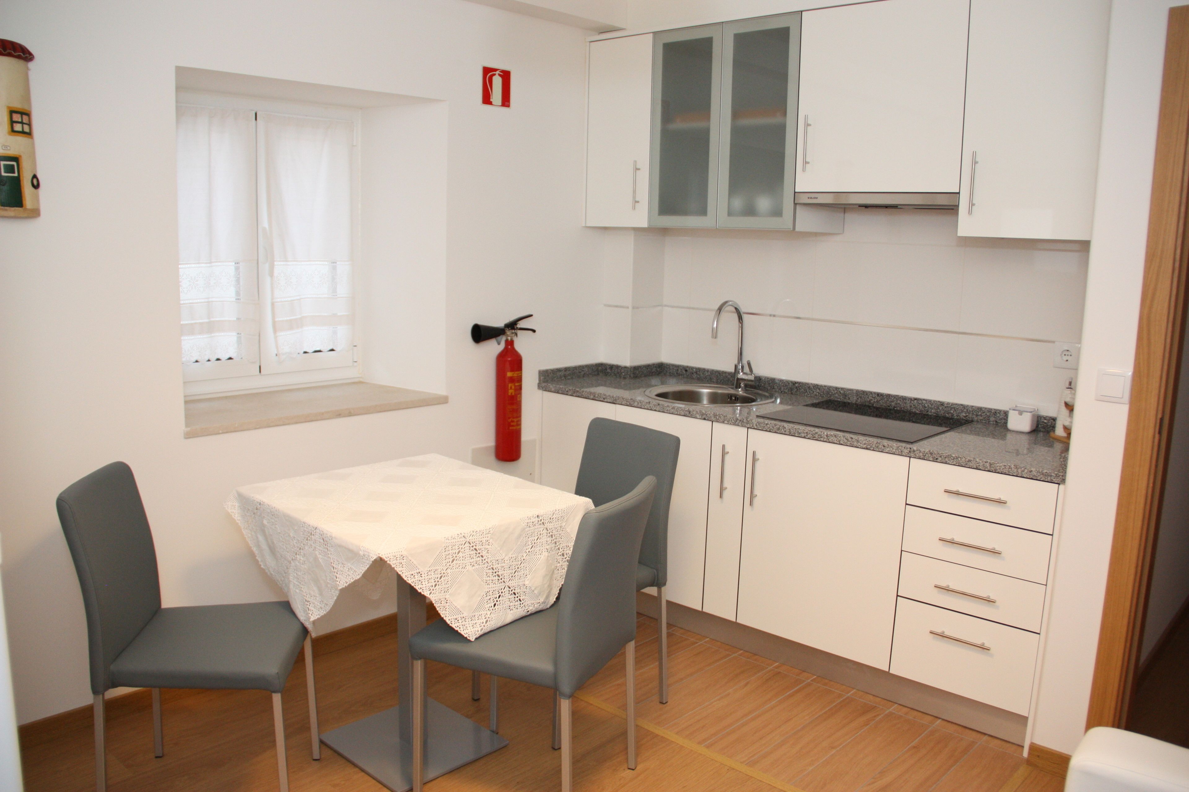 A small kitchenette with a sink, a window with curtains, and a table with chairs.