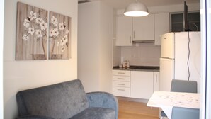 A modern kitchen with white cabinets, a dining table with chairs, and a gray sofa. - Pátio da Caetana (Almeida)