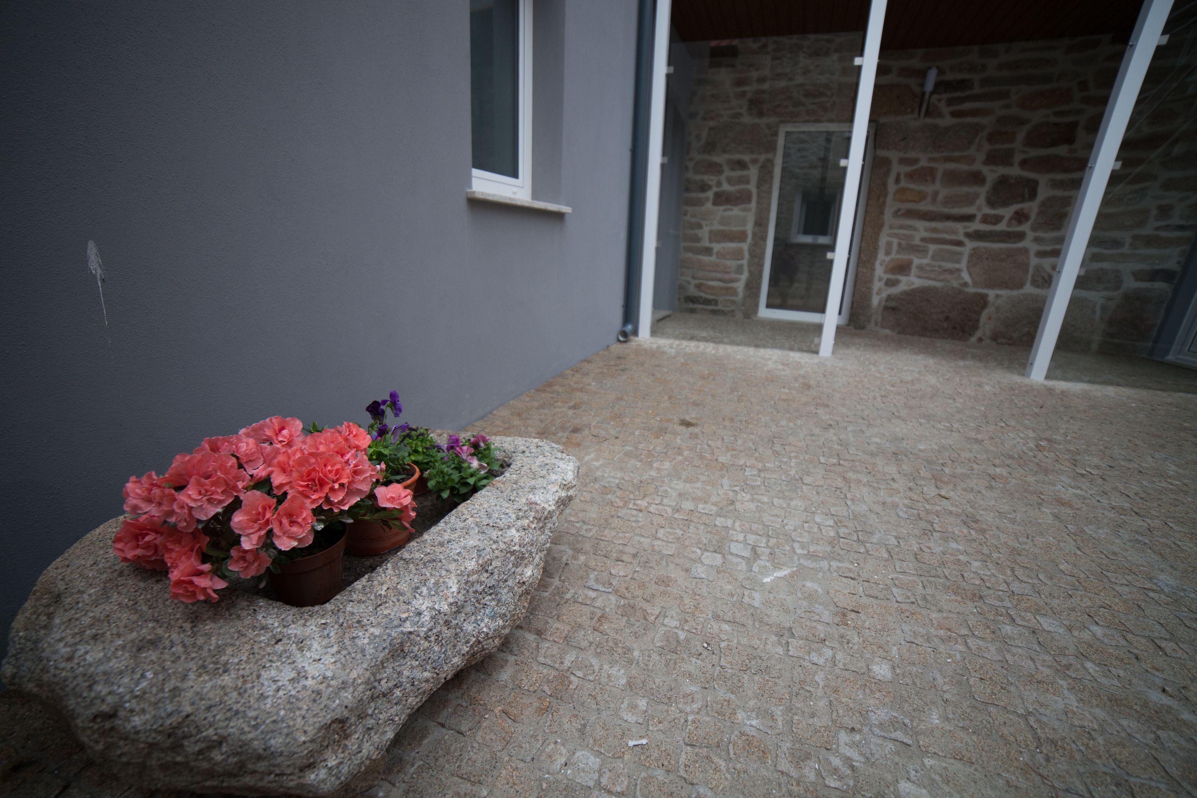 A stone planter with pink and purple flowers on a paved patio.
