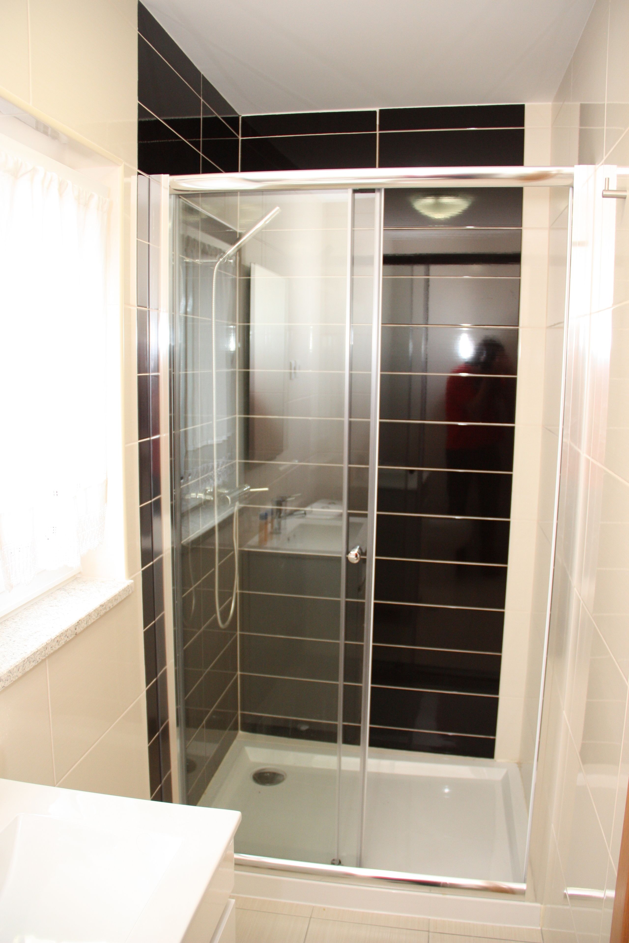 A glass-enclosed shower stall with a white sink and a window to the left.