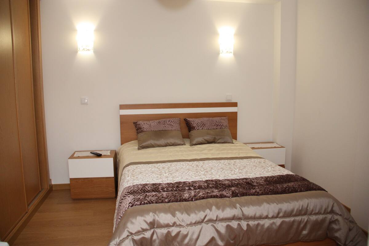 A neatly arranged bedroom with a wooden headboard, two bedside tables, and a bed with a patterned bedspread.