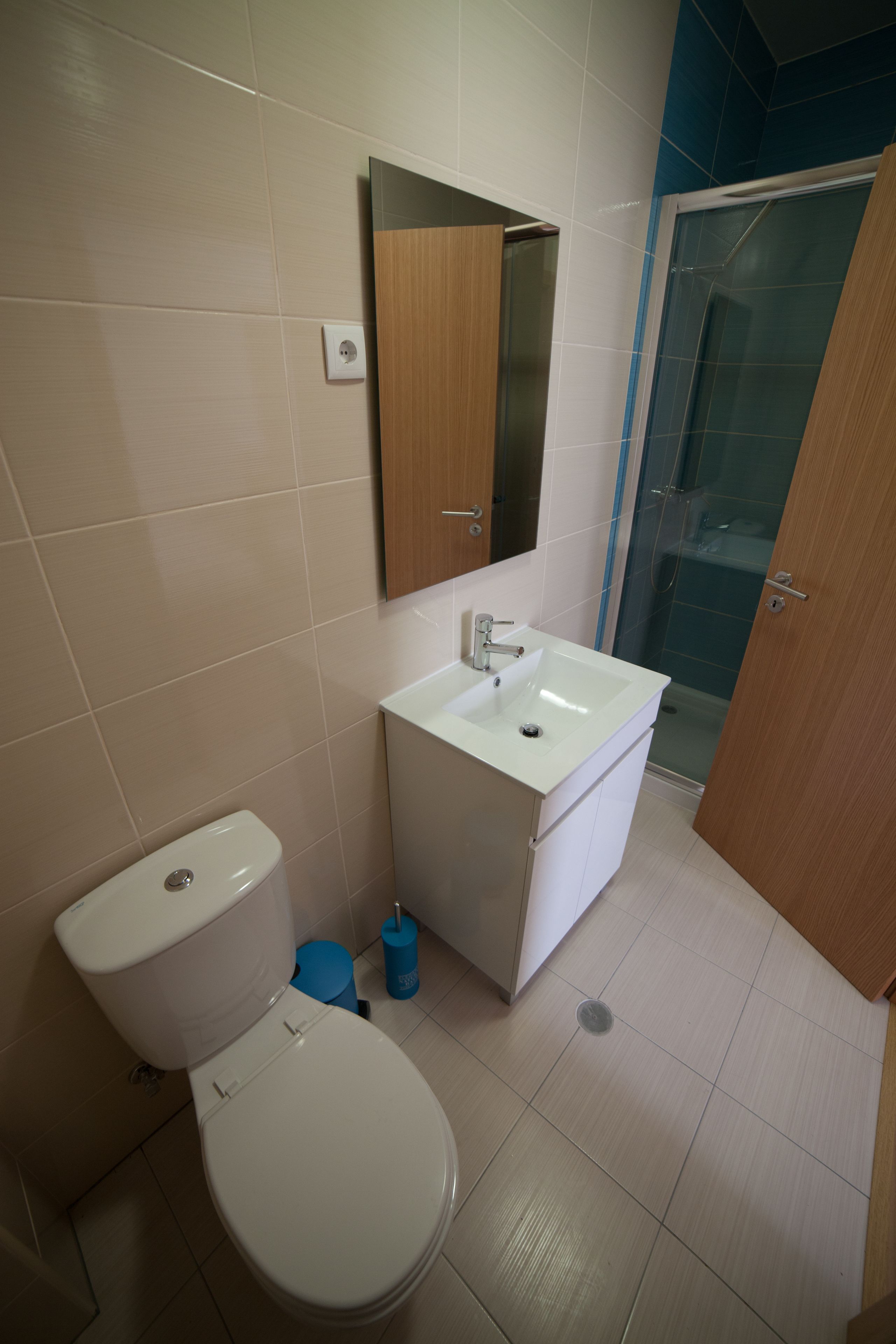 A bathroom with a toilet, sink, mirror, and shower area.