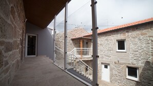 A stone building with a staircase leading to a second floor, a wooden ceiling, and a clear sky. - Pátio da Caetana (Almeida)