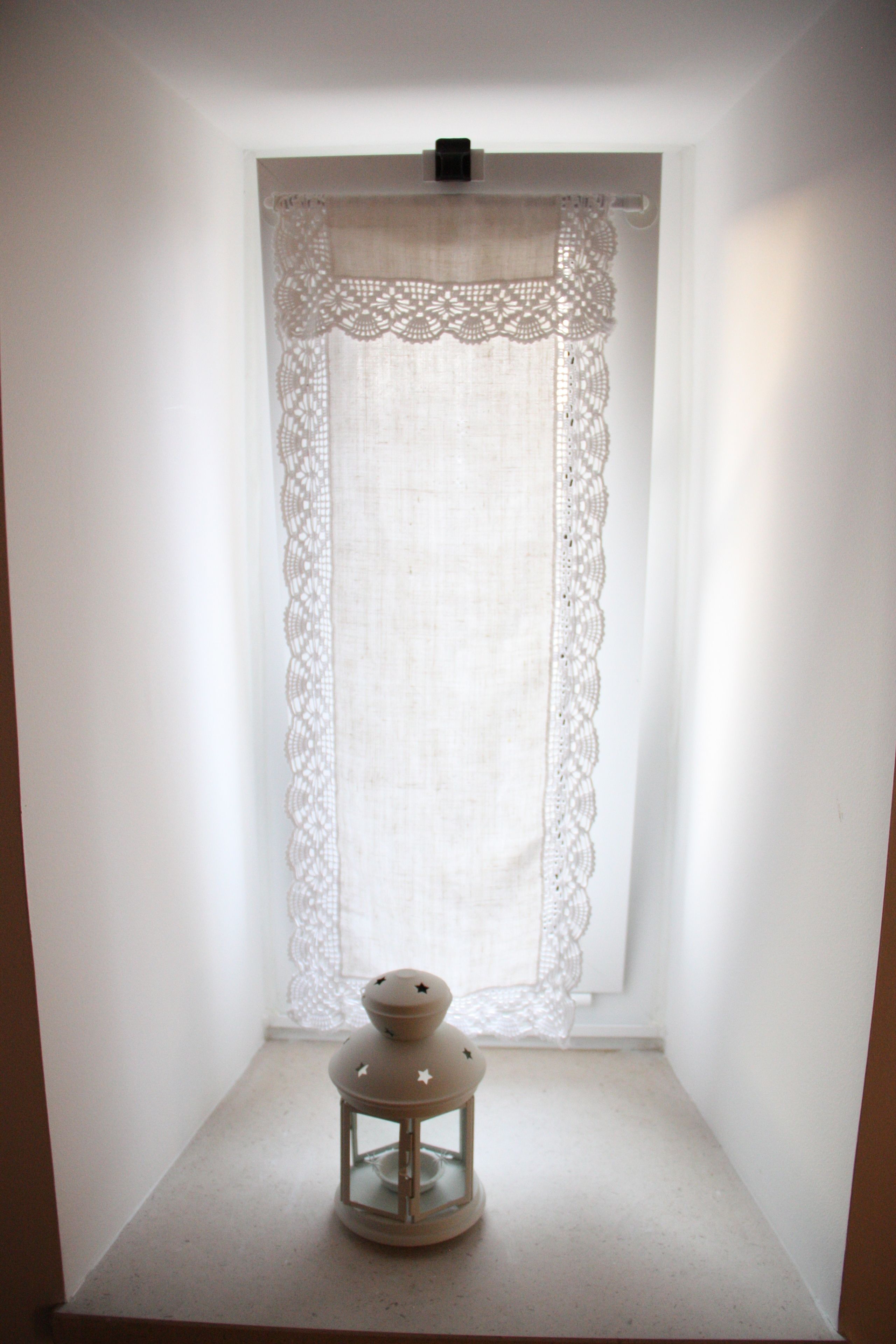 A corner with a white curtain, a small table, and a lantern.