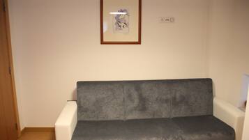 A room with a grey sofa against a white wall, a framed picture above the sofa, and a wooden door on the left.