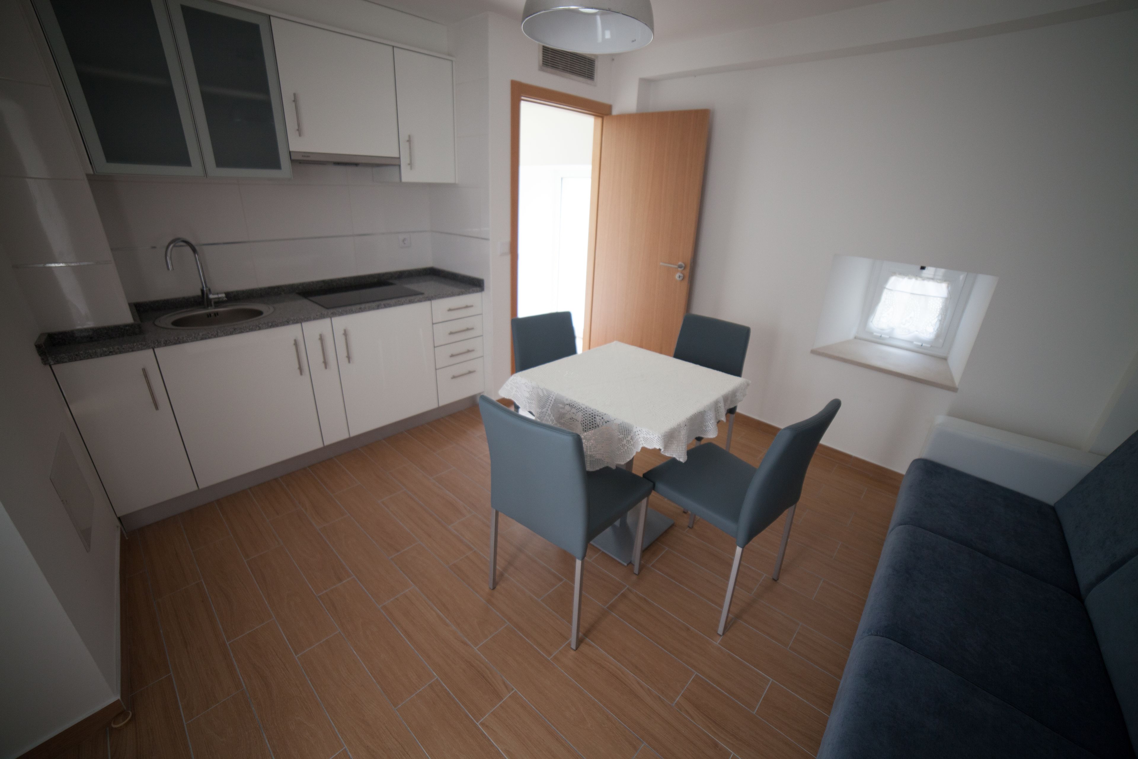 Una cocina compacta con armarios blancos, un lavamanos y una zona de comedor con mesa y sillas.